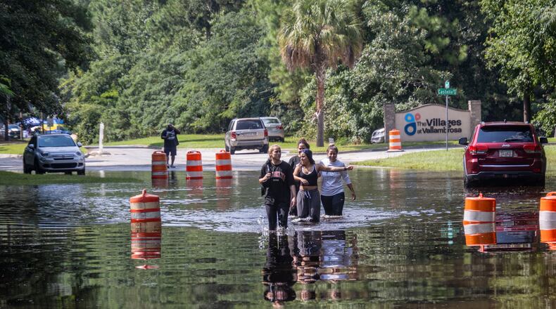 A group of people walk through a flooded road on Bradley Boulevard on Monday in Savannah. (AJC Photo/Katelyn Myrick)