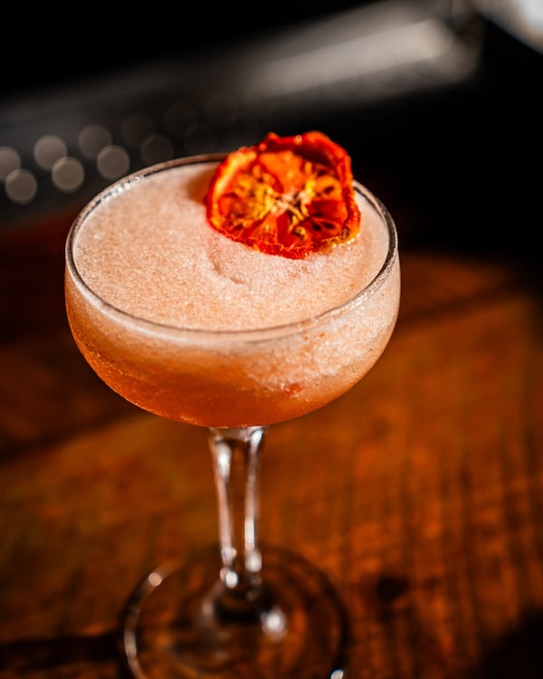 A frothy cocktail served in a coupe glass with a matching flower as garnish.