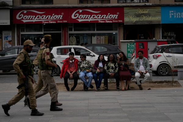 Indian tourists rests on a bench as policemen guard near a clock tower at city centre in Srinagar, Indian controlled Kashmir,Tuesday, April. 22, 2025. (AP Photo/Mukhtar Khan)