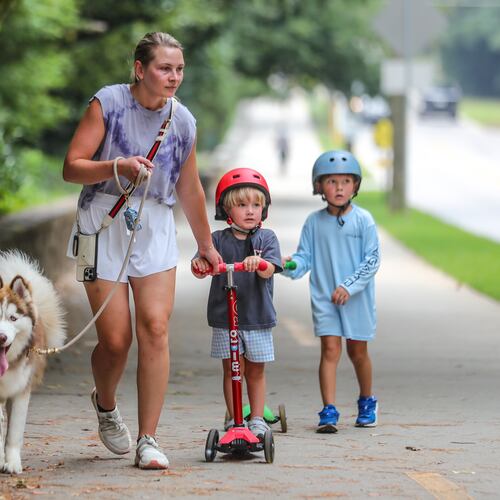 July 17, 2023 Atlanta: Madison Langston holds onto husky, Bosley (left) as 3-year old Charlie (center) and brother, Petey-4 (right) make their way along the long sidewalk at Chastain Park in Atlanta on Monday, July 17, 2023. (John Spink / John.Spink@ajc.com)