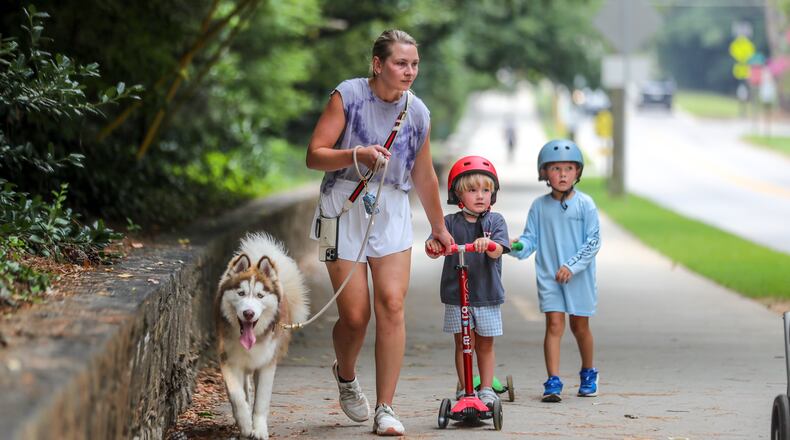 July 17, 2023 Atlanta: Madison Langston holds onto husky, Bosley (left) as 3-year old Charlie (center) and brother, Petey-4 (right) make their way along the long sidewalk at Chastain Park in Atlanta on Monday, July 17, 2023. (John Spink / John.Spink@ajc.com)