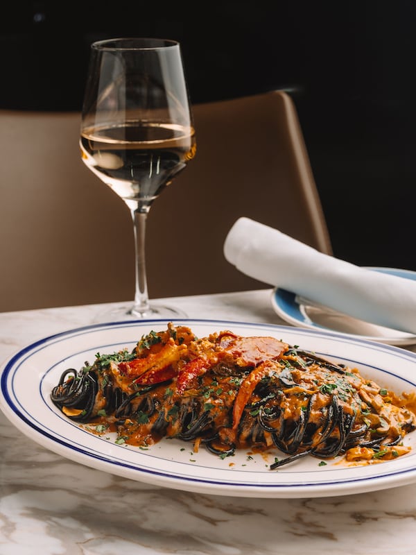 A plate of squid ink spaghetti flanked by a glass of white wine