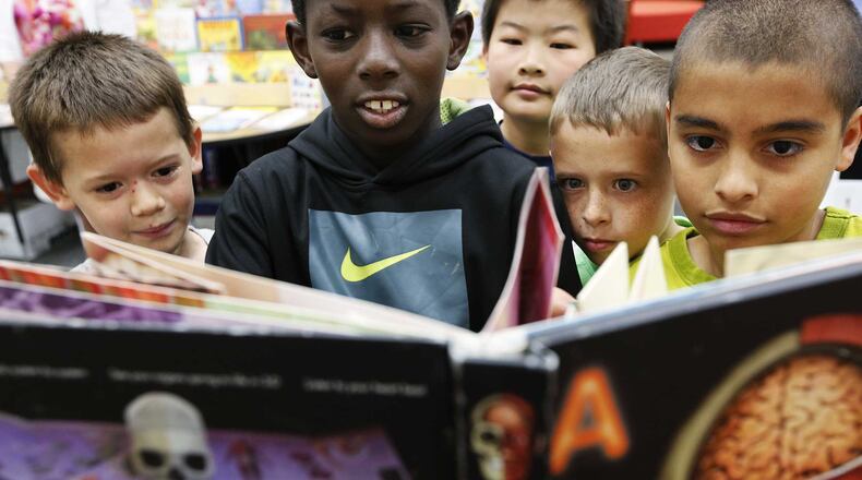 Fourth graders at a book fair at their school media center are fascinated by a science book.