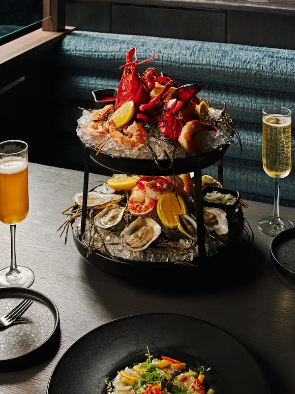 A large seafood tower on a restaurant table with lobster, shrimp, oysters, lemons and other items on ice, flanked by flutes of sparkling wine on either side.