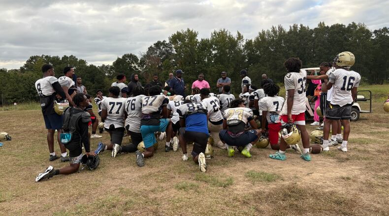 Hapeville Charter players huddle up after a practice in October 2025. Coach Winston Gordon (center in navy polo shirt and cap) has been the team's coach since its first varsity season in 2011, leading the Hornets to 10 consecutive playoff berths, five region titles and a Class 2A state championship. Former player Arden Key, now with the Tennessee Titans, described the team's practice field as "a concrete jungle." (Ken Sugiura/AJC)