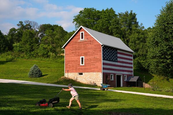 Stacey Schmitt mows in front of a flag-painted barn Saturday, June 7, 2025, on her family farm near Linwood, Kan. (AP Photo/Charlie Riedel)