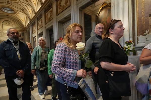 A woman holds a white rose as she waits in line to pay her respects to the tomb of Pope Francis inside St. Mary Major Basilica in Rome, Sunday, April 27, 2025. (AP Photo/Alessandra Tarantino)