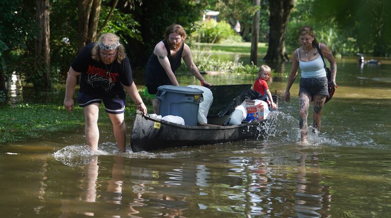 Scott Conrad, left, Joseph Workman, second from left, Ronan Carey, in the boat, and Kesley Patterson use a kayak to transport items from their flooded homes in Indianapolis, Sunday, Aug. 16, 2026. (AP Photo/Obed Lamy)