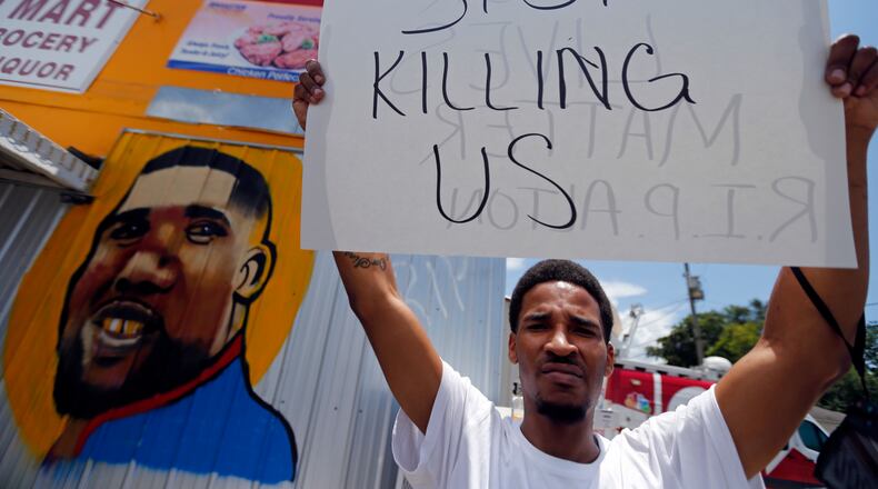 A man holds a sign in front of a mural of Alton Sterling while attorneys, not pictured, speak in front of the Triple S Food Mart in Baton Rouge, La., Thursday, July 7, 2016. Sterling, 37, was shot and killed outside the convenience store by Baton Rouge police, where he was selling CDs. (AP Photo/Gerald Herbert)