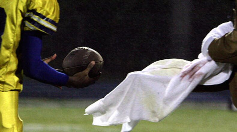 Southwest Dekalb coaches dry balls for their quarterbacks during pre-game practice as a misting rain kept the field, spectators and players damp at Marist.