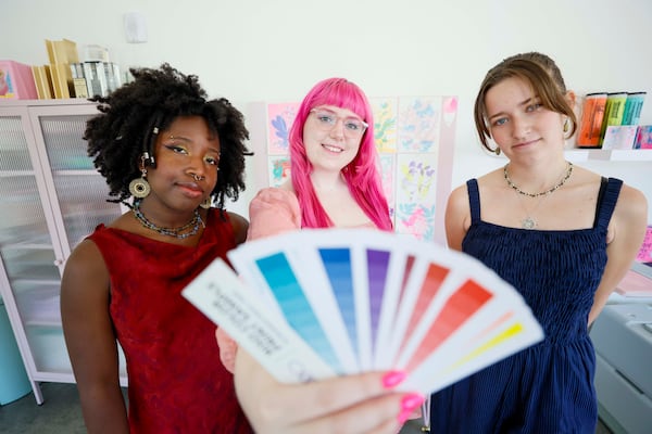 Samantha Richardson (center) — with Arantza Peña Popo (left) and Maddy Lyons — holds a fan deck, a reference tool for graphic designers and other creatives that shows the vibrant spot colors available in Risograph printing at Posy Press. (Miguel Martinez/AJC)