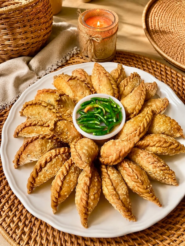 Fried pastel dumplings arranged around a bowl of green dipping sauce.