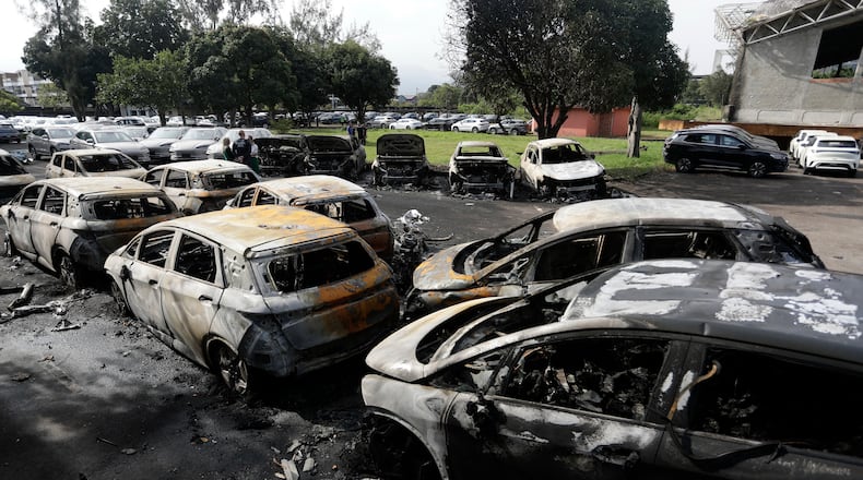 Burned vehicles fill a car dealership parking lot where, according to police, two helicopters collided in midair and crashed in Rio de Janeiro, Brazil, Sunday, June 14, 2026. (AP Photo/Bruna Prado)