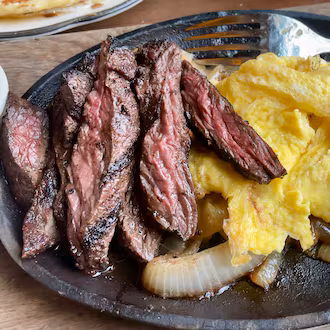 A cast iron plate with sliced steak and scrambled eggs