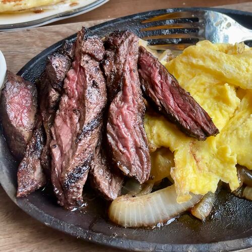 A cast iron plate with sliced steak and scrambled eggs