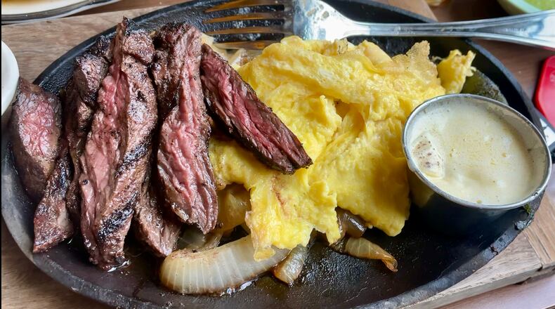 A cast iron plate with sliced steak and scrambled eggs