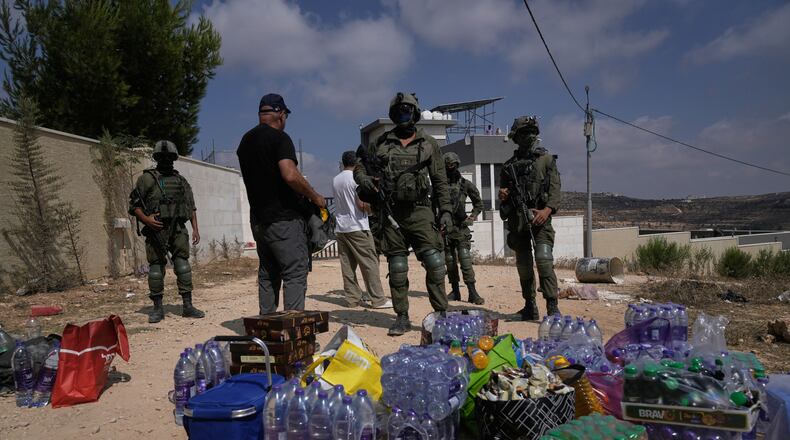 Activists accumulate food and water supplies in front of Israeli army soldiers who are blocking the road leading to the houses of three Palestinian families that have been besieged by Israeli settlers for six days, in the occupied West Bank village of Qusra, south of Nablus, Friday, Aug. 14, 2026. (AP Photo/Majdi Mohammed)