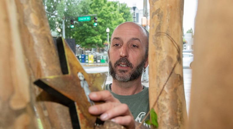 Atlanta artist Larry Holland hides a piece of his artwork in a tree in downtown Decatur last month. He is involved with FAFATL (Free Friday Art Atlanta), a citywide art scavenger hunt. Artists hide artwork then post a picture on social media so seekers can find it. Contributed by Phil Skinner