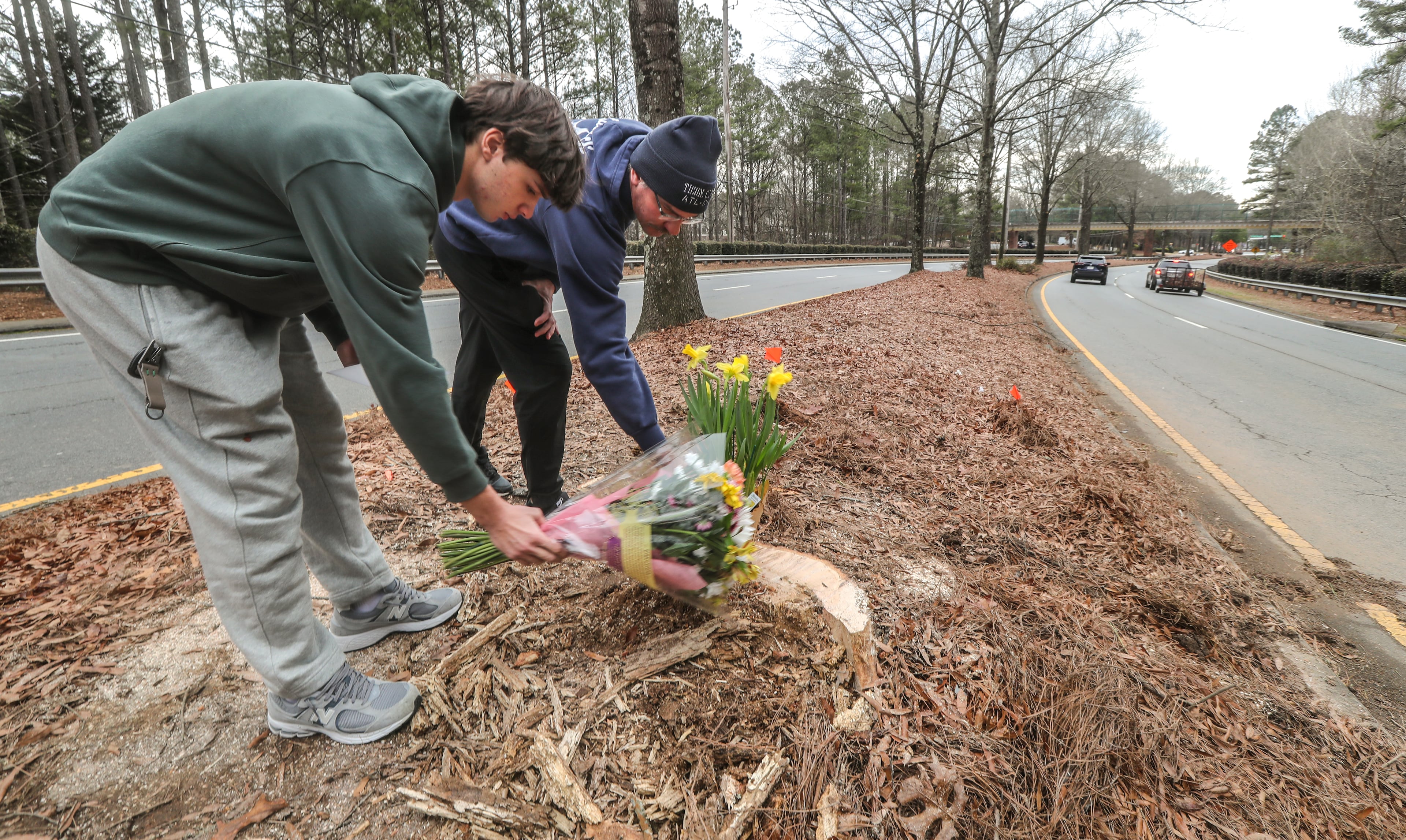 John Kopach and son, Oliver Kopach, leave flowers at the site where a car carrying five teens crashed, killing two of them in Cherokee County in January 2024. (AJC file)