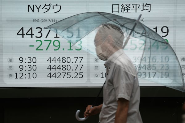 A person walks in front of an electronic stock board showing Japan's Nikkei and New York Dow indexes at a securities firm Monday, July 14, 2025, in Tokyo. (AP Photo/Eugene Hoshiko)