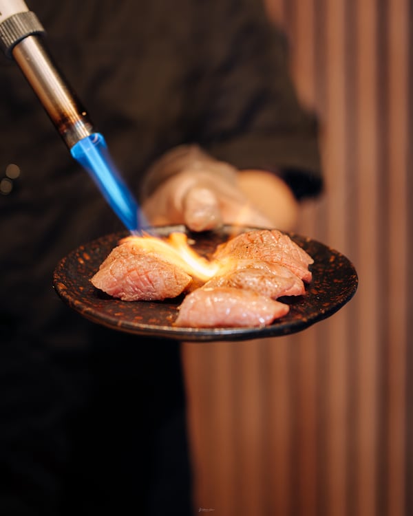 A chef at 1678 Omakase uses a blowtorch to lightly cook pieces of nigiri.