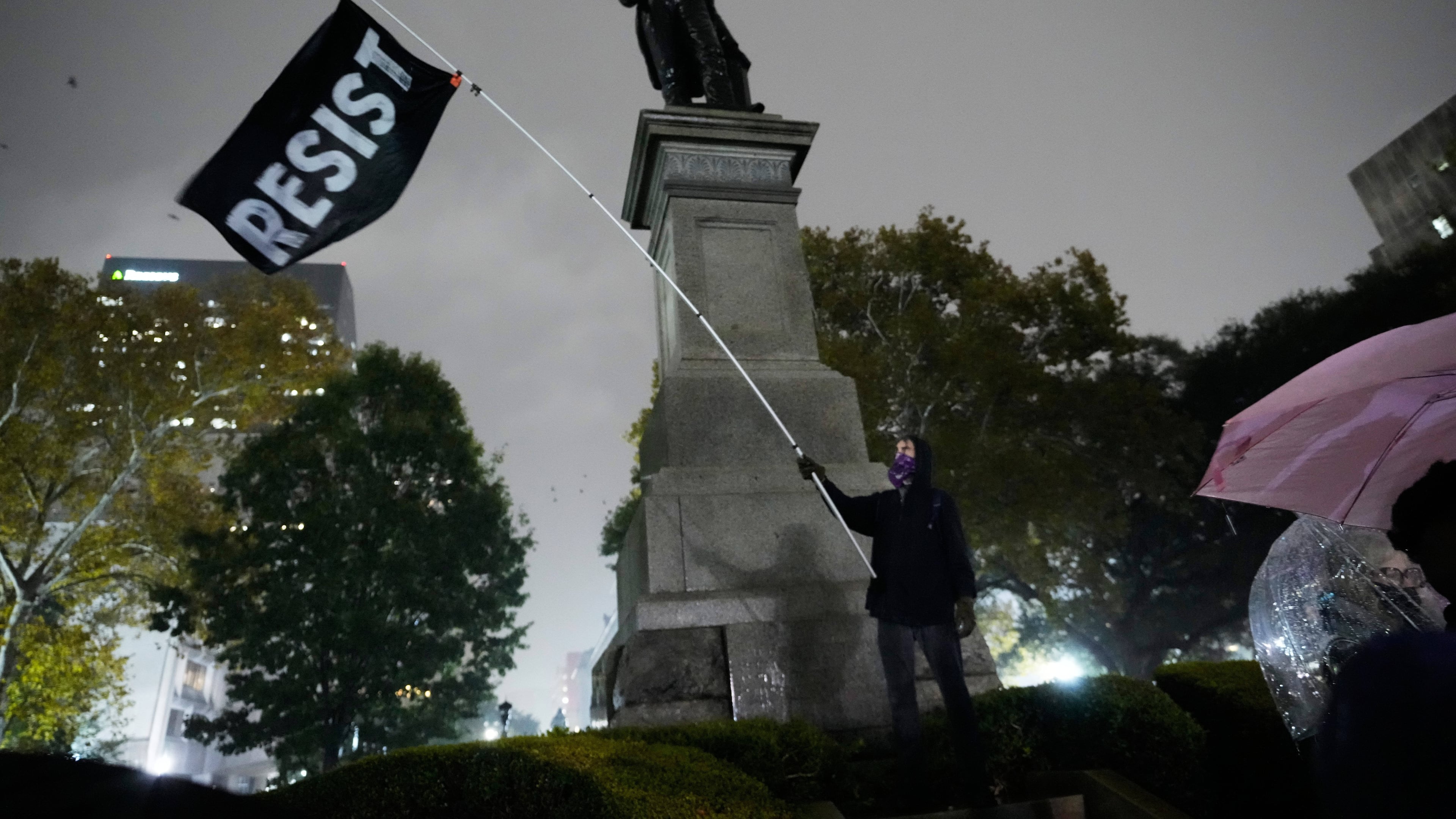 A protestor waves a flag in a pouring rain during a demonstration against an impending Customs and Border Patrol immigration crackdown in New Orleans, Monday, Dec. 1, 2025. (AP Photo/Gerald Herbert)