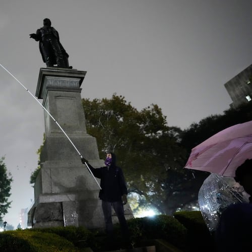 A protestor waves a flag in a pouring rain during a demonstration against an impending Customs and Border Patrol immigration crackdown in New Orleans, Monday, Dec. 1, 2025. (AP Photo/Gerald Herbert)