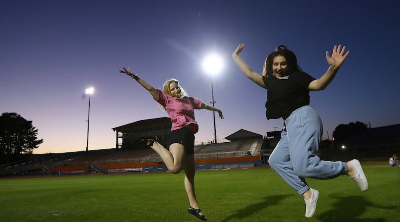 Graduating seniors Megan Hollister (left) and Caitlyn Bradley jump while setting their cell phones on the grass and filming a video of themselves in the Big Orange Jungle and Hugh Buchanan Field as it is lit up to symbolize the class of 2020 is a light to the community at Parkview High School on Tuesday, April 14, 2020, in Lilburn. Every week night at 8:20 pm (20:20 military time) Athletic Director Nick East turns on the scoreboard and stadium lights for 20 minutes and 20 seconds to honor the class of 2020.