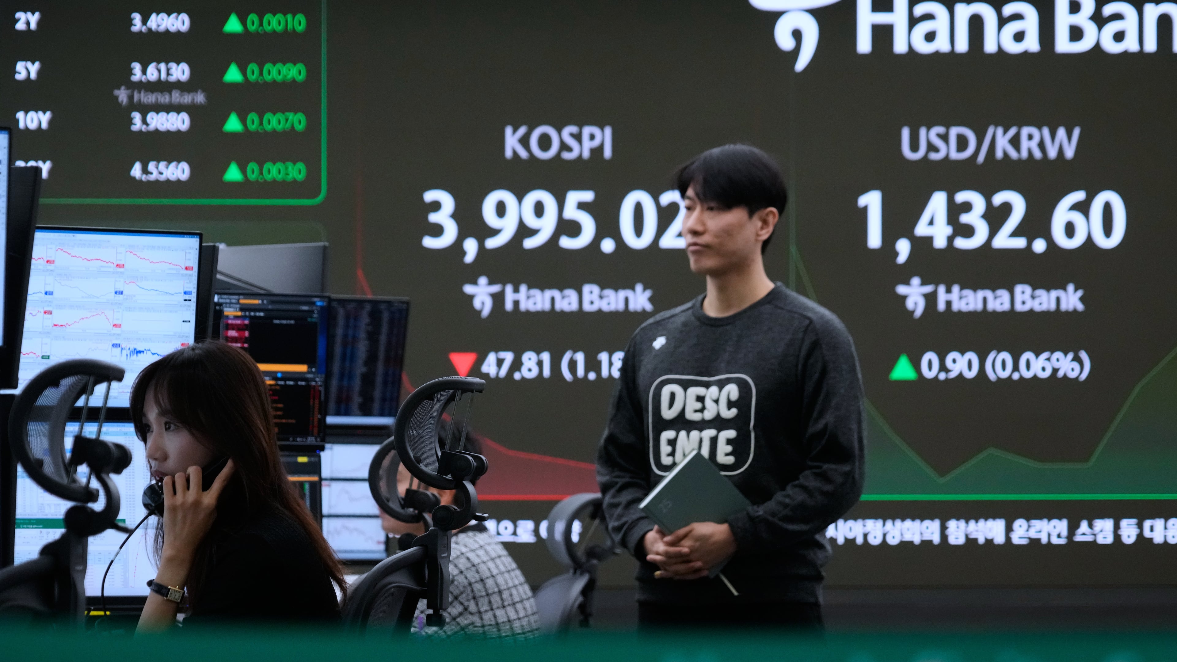 A currency trader talks on the phone near a screen showing the Korea Composite Stock Price Index (KOSPI) and the foreign exchange rate between U.S. dollar and South Korean won, right, at the foreign exchange dealing room of the Hana Bank headquarters in Seoul, South Korea, Tuesday, Oct. 28, 2025. (AP Photo/Ahn Young-joon)