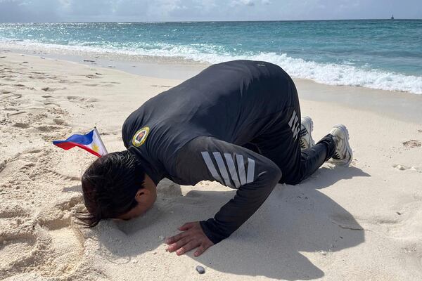 Armed Forces of the Philippines spokesperson Col. Francel Margareth Padilla kisses the beach after alighting from a motorboat with other visitors at the Philippine-occupied West York island, locally known as Likas, at the disputed South China Sea on June 5, 2025. (AP Photo/Jim Gomez)