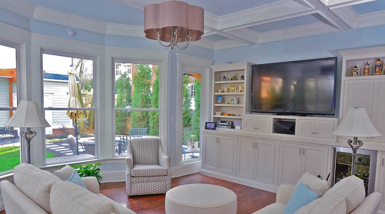 Built-in bookshelves and a sectional wrap around the great room. The shelves were designed to accommodate the flat-screen TV from their previous home.The coffered ceiling adds dimension while the expansive open windows offer a view to the backyard.