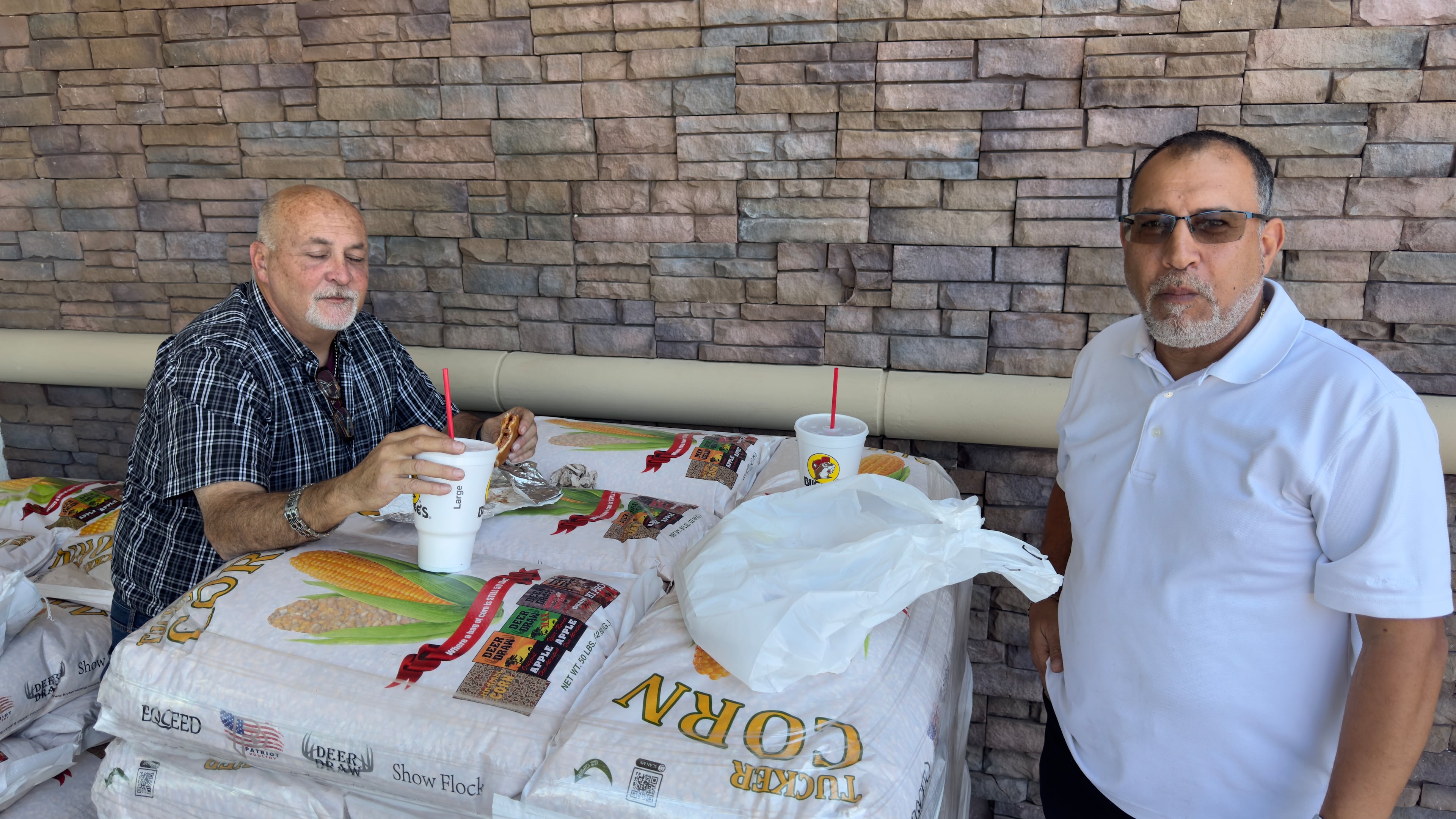 Bassem Zakhary, left, and Jorge Alvarez, of Florida, eat lunch on a pallet of Buc-ee’s Deer Corn at the convenience superstore’s Warner Robins location. (Joe Kovac Jr./AJC)