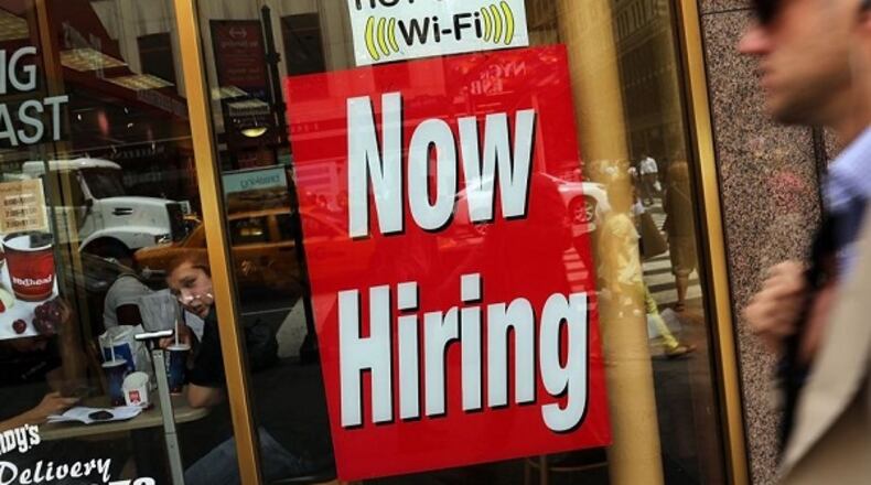 A "now hiring" sign is viewed in the window of a business.