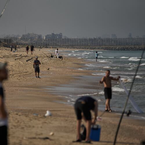 Backdropped by buildings destroyed during Israeli ground and air operations in the northern Gaza Strip, people walk and fish at Zikim Beach, near Ashkelon, in southern Israel, Friday, Oct. 17, 2025. (AP Photo/Leo Correa)
