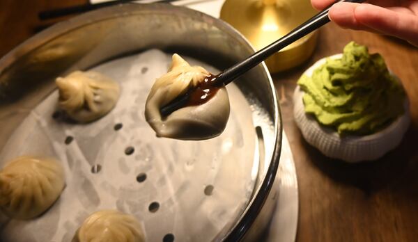 A soup dumpling filled with chocolate, held by a pair of chopsticks, with a matcha whip cream dipping sauce in the background.