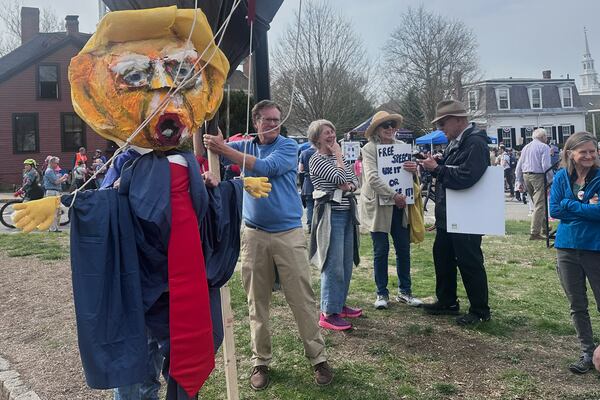 Protesters walk behind a parade honoring the 250th anniversary of the American Revolution, Saturday, April 19, 2025, in Concord, Mass. (AP Photos/Michael Casey)
