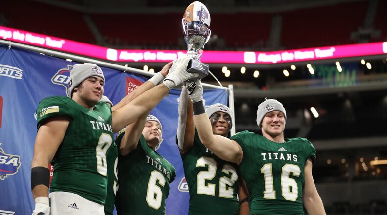Class AAAA champions: Blessed Trinity players (from left) Jr Bivens (8), Ryan Davis (6), Steele Chambers (22), and JD Bertrand (16) celebrate with the state championship trophy after their 23-9 win against Cartersville at Mercedes-Benz Stadium Wednesday, December 12, 2018, in Atlanta. (Jason Getz/Special)