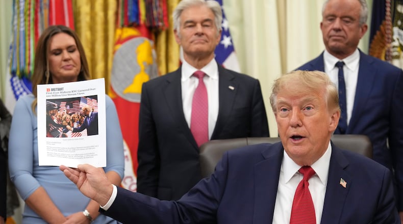 President Donald Trump holds up a printout of a Breitbart article as Arkansas Gov. Sarah Huckabee Sanders, from left, Mehmet Oz, administrator of the Centers for Medicare & Medicaid Services, and Health and Human Services Secretary Robert F. Kennedy Jr., look on during an event about healthcare in the Oval Office of the White House, Friday Sept. 18, 2026, in Washington. (AP Photo/Jacquelyn Martin)