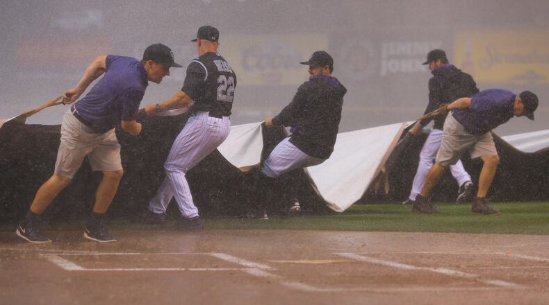 Manager Walt Weiss, catcher Michael McKenry #8 and starting pitcher Chad Bettis #35 of the Colorado Rockies help the grounds crew pull the tarp over the field during a could burst that halted play against the Atlanta Braves in the first inning at Coors Field on July 9, 2015 in Denver, Colorado. (Photo by Justin Edmonds/Getty Images)