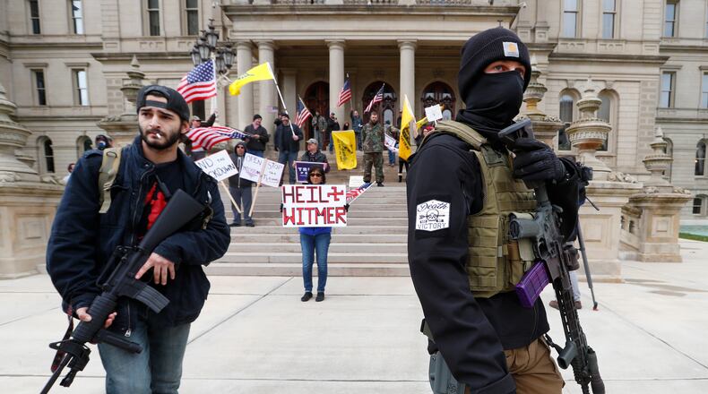 Protesters carry rifles near the steps of the Michigan State Capitol building in Lansing, Mich., Wednesday, April 15, 2020. Flag-waving, honking protesters drove past the Michigan Capitol on Wednesday to show their displeasure with Gov. Gretchen Whitmer's orders to keep people at home and businesses locked during the new coronavirus COVID-19 outbreak. (AP Photo/Paul Sancya)