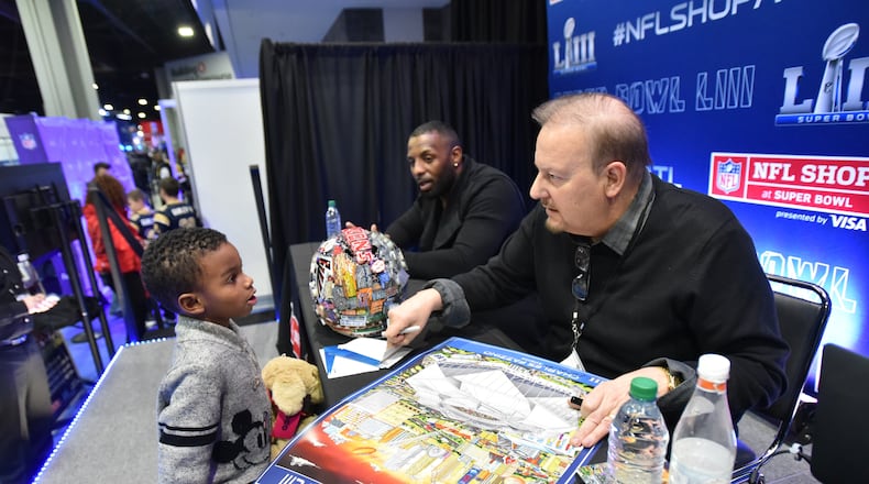 The NFL's official Super Bowl artist Charles Fazzino signs an autograph for fan Kingston Morton at the NFL shop during Super Bowl Experience inside the Georgia World Congress Center on Wednesday, January 30, 2019.