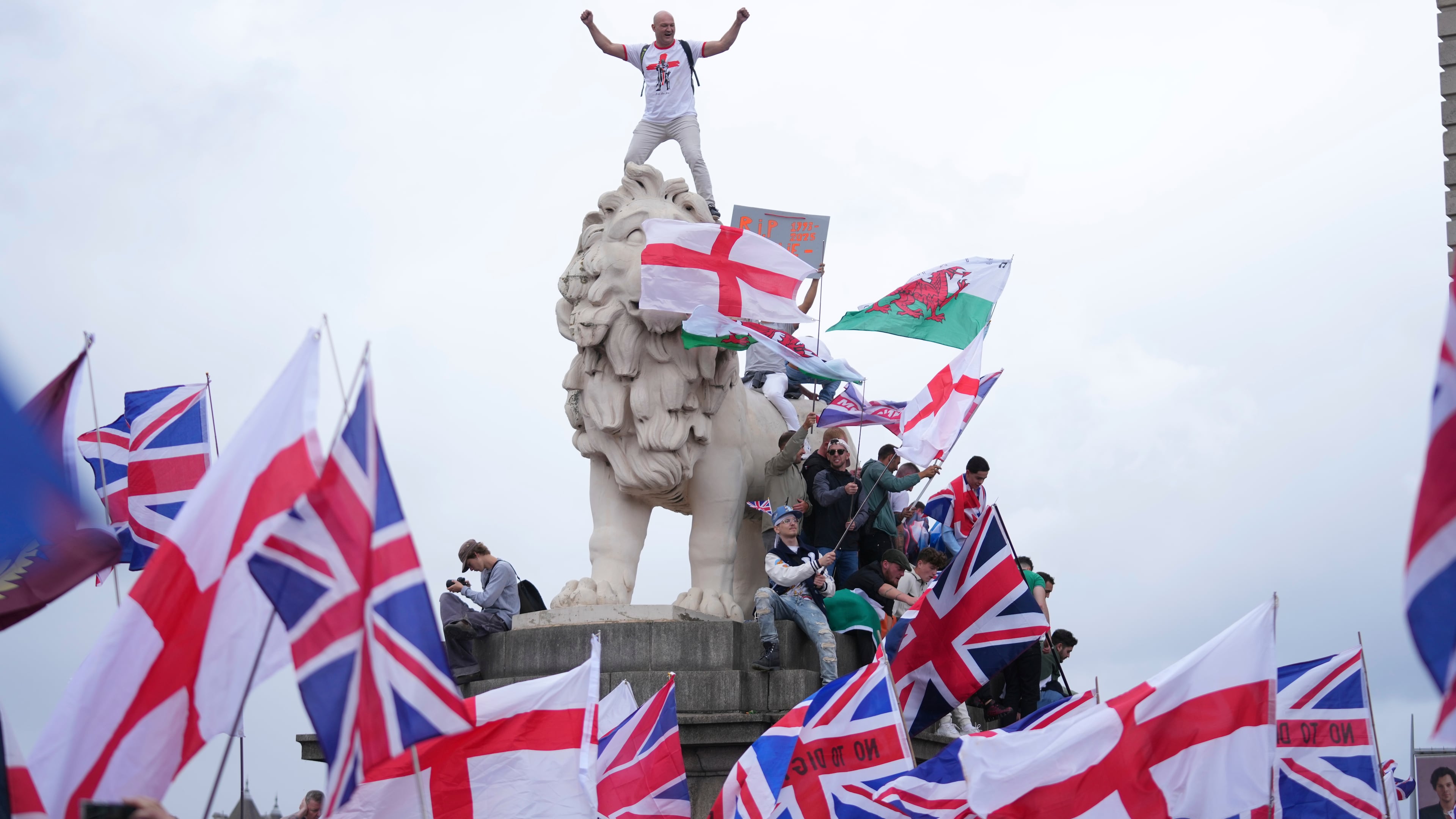 A demonstrator stands on the head of one of the lions of Westminster Bridge during a Tommy Robinson-led Unite the Kingdom march and rally in London, Saturday Sept. 13, 2025. (AP Photo/Joanna Chan)