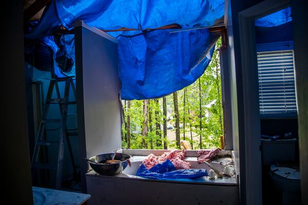 Sherell Lewis used a blue tarp to stop water from entering his house after a tree caused damage to the master bathroom in his southwest Atlanta neighborhood Monday.