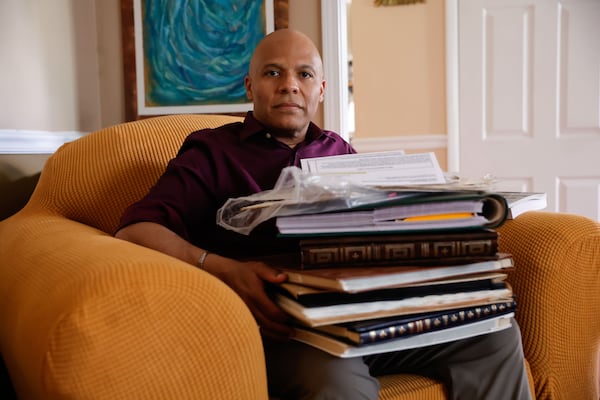 Ken Oglesby, the family historian of the Cloud-Travis family poses for a photo while holding family photo albums at his home in Alpharetta on Monday, June 30, 2025. (Natrice Miller/AJC)