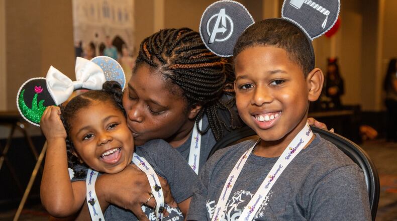 Kiki Troutman, 5, gets a kiss from her mother, Teneaski, while her brother Keon smiles as families gather at the Hilton Atlanta Airport the night before heading to Disney World for 2020 Bert’s Big Adventure. Photo by Phil Skinner