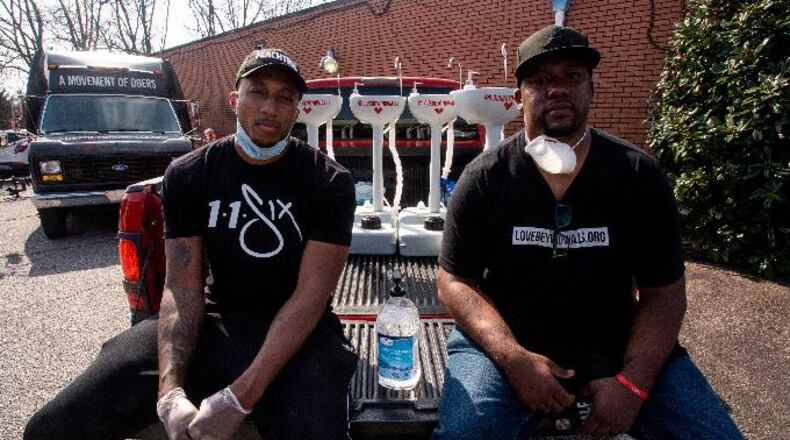 Hip hop recording artist Lecrae, left, and Love Beyond Walls founder Terence Lester, right, sit on a truck bed filled with portable wash stations on Thursday, March 19, 2020 in College Park, Georgia. The wash stations were distributed by Lecrae and volunteers with Love Beyond Walls, a non-profit, throughout Atlanta in areas with a high density of homeless persons. (AP Photo/ Ron Harris)