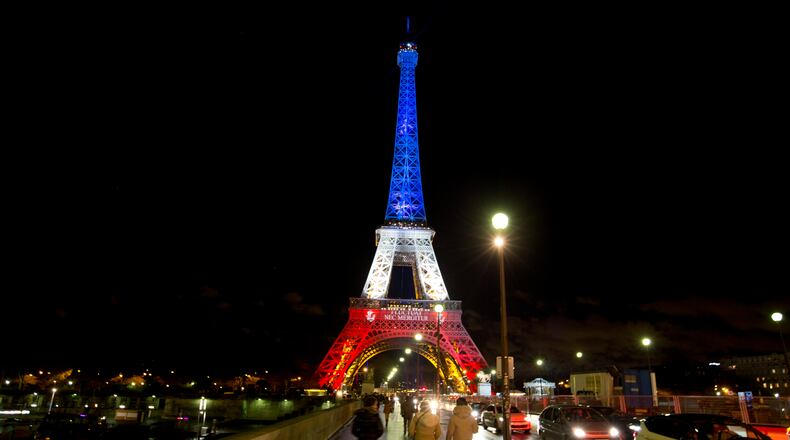 People walk towards the illuminated Eiffel Tower in the French national colors red, white and blue in honor of the victims of the attacks in Paris, Tuesday, Nov. 17, 2015. France is demanding security aid and assistance from the European Union in the wake of the Paris attacks and has triggered a never-before-used article in the EU's treaties to secure it. (AP Photo/Peter Dejong)