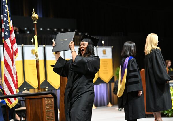 A graduate reacts as she receives her diploma during Kennesaw State University’s spring commencement ceremony at the KSU Convocation Center in May. (Hyosub Shin/AJC)
