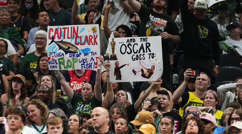 Fans wave signs referencing Indiana Fever guard Caitlin Clark during the second half of a WNBA basketball game between the Seattle Storm and the Indiana Fever, Tuesday, July 28, 2026, in Seattle. (AP Photo/Lindsey Wasson)