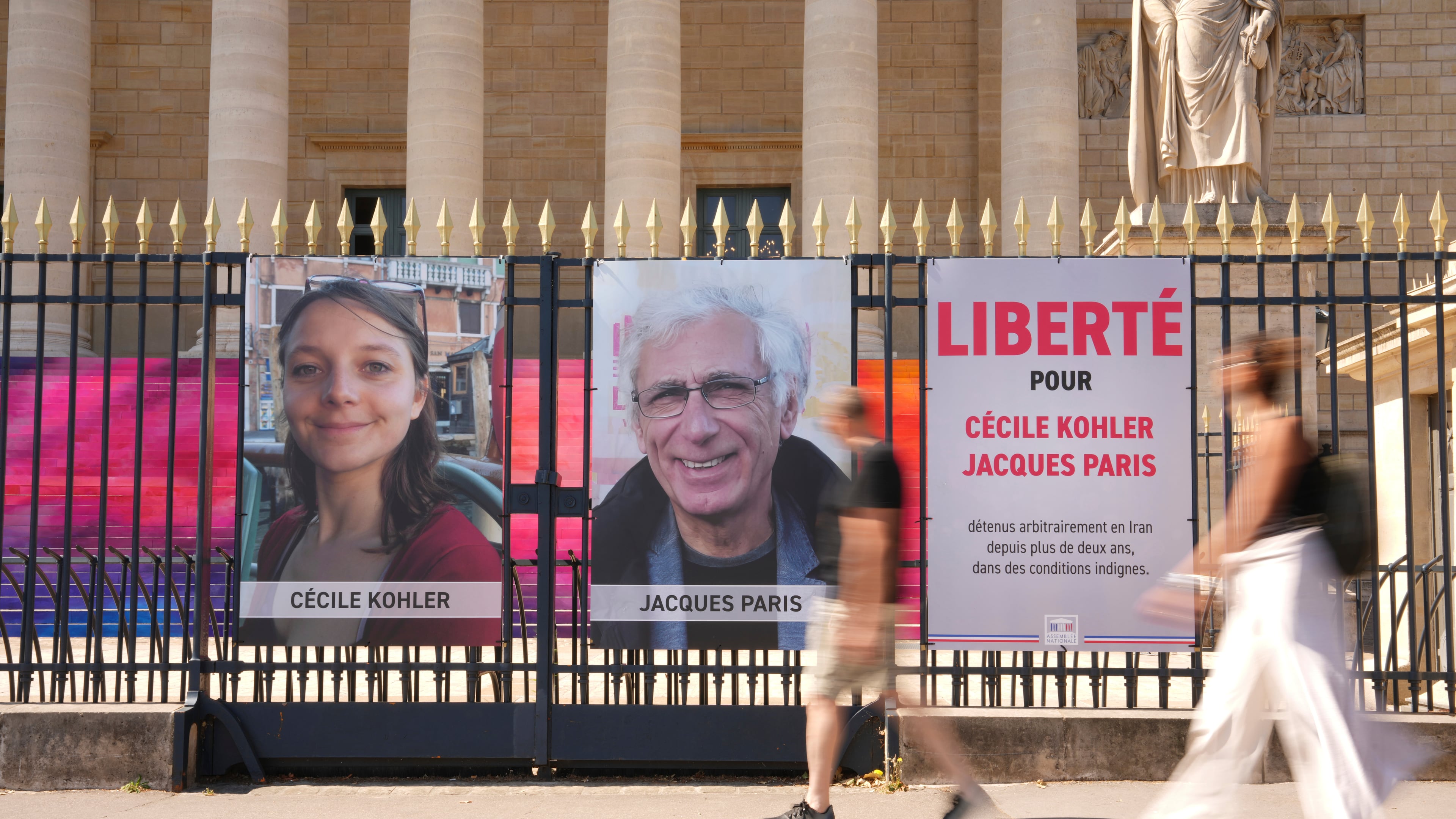 FILE - People walk past the portraits of French nationals Cecile Kohler and Jacques Paris in front of the French National Assembly in Paris on July 3, 2025. (AP Photo/Aurelien Morissard, File)